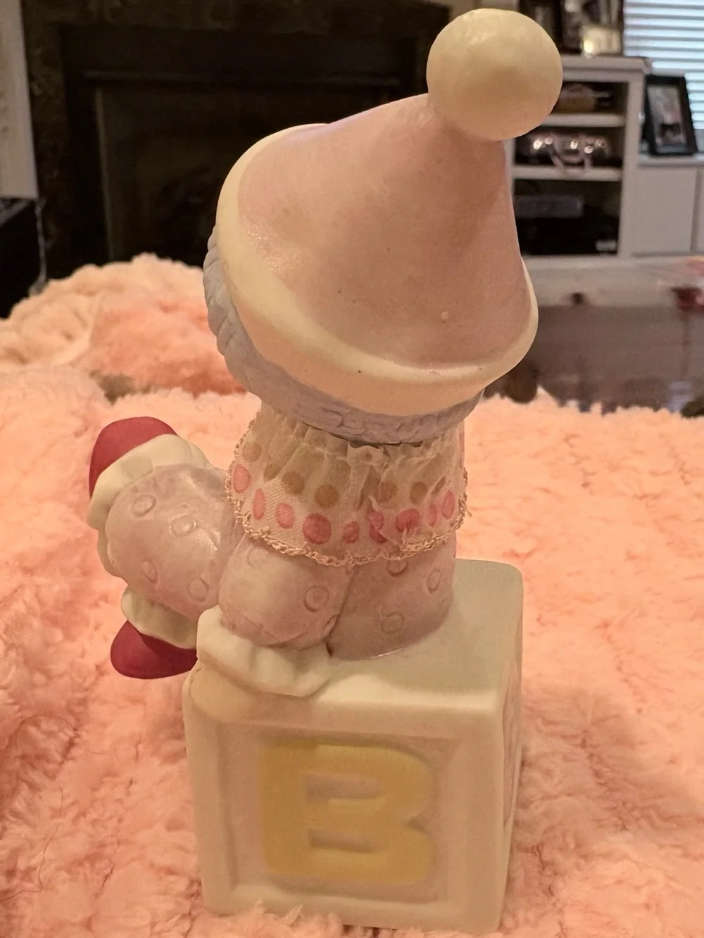 Hand -painted pastel pink-clad baby clown wearing a textured hat.
